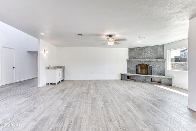 unfurnished living room with a fireplace, a textured ceiling, light wood-type flooring, and ceiling fan