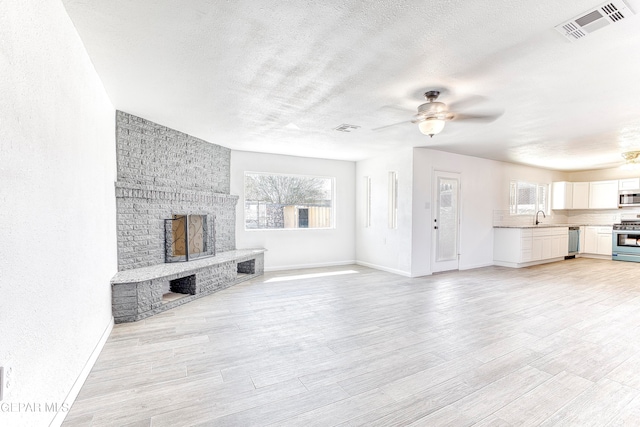 unfurnished living room featuring light wood-type flooring, a fireplace, ceiling fan, and a textured ceiling