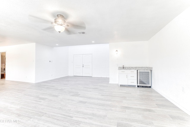 unfurnished living room with ceiling fan, beverage cooler, and light hardwood / wood-style floors