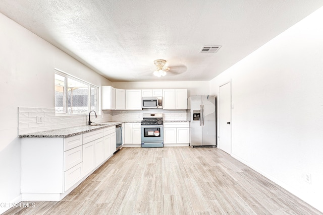 kitchen featuring white cabinets, sink, appliances with stainless steel finishes, dark stone counters, and light hardwood / wood-style floors