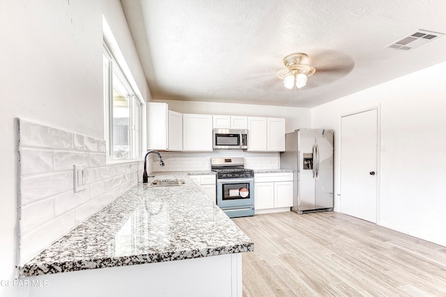 kitchen featuring light stone counters, sink, white cabinetry, stainless steel appliances, and light hardwood / wood-style floors