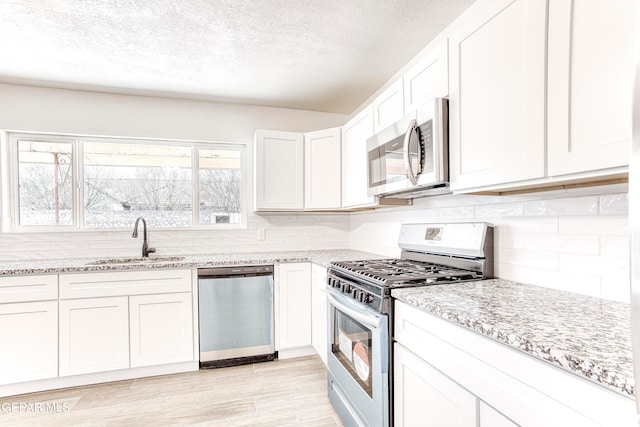 kitchen with light stone countertops, stainless steel appliances, white cabinets, sink, and light hardwood / wood-style floors