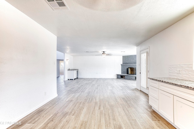 unfurnished living room featuring a fireplace, light hardwood / wood-style floors, a textured ceiling, and ceiling fan