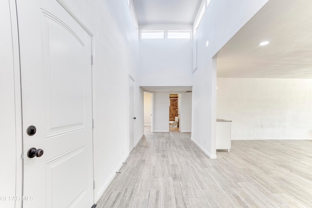 hall with a high ceiling and light hardwood / wood-style floors