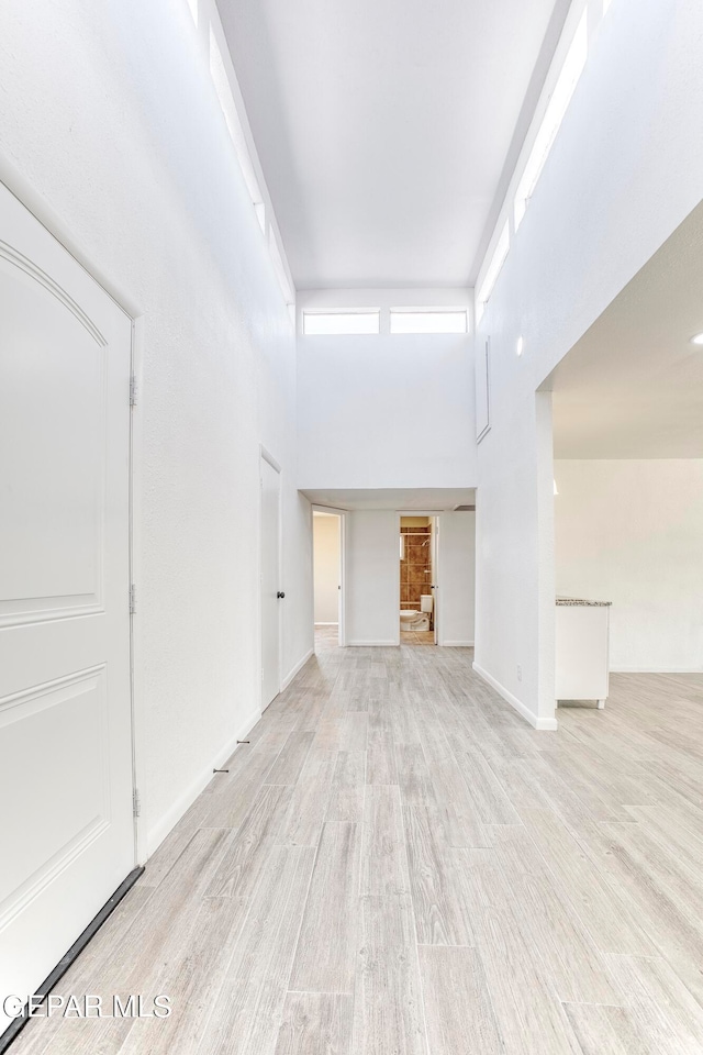 unfurnished living room with light wood-type flooring and a towering ceiling