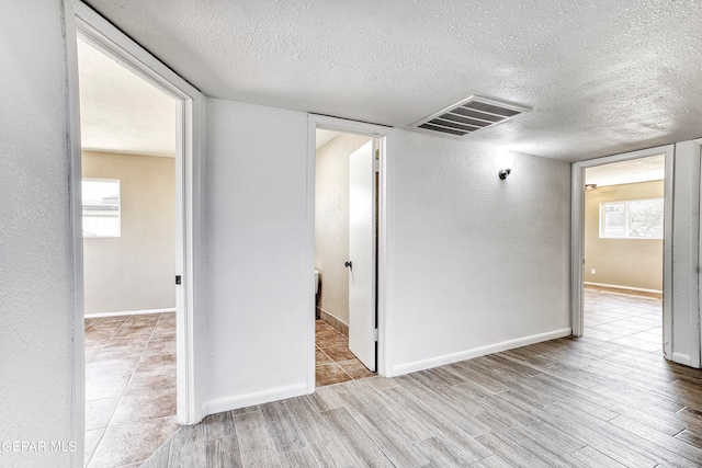 empty room featuring plenty of natural light, light hardwood / wood-style floors, and a textured ceiling