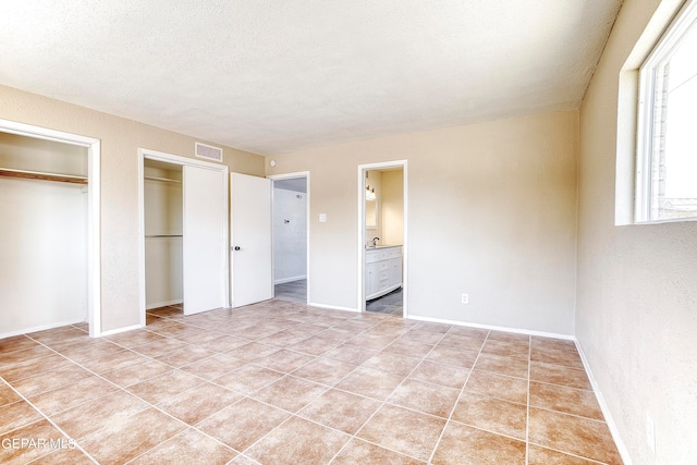 unfurnished bedroom with light tile patterned flooring, multiple closets, connected bathroom, and a textured ceiling