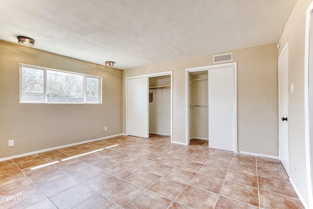 unfurnished bedroom featuring two closets, light tile patterned floors, and a textured ceiling