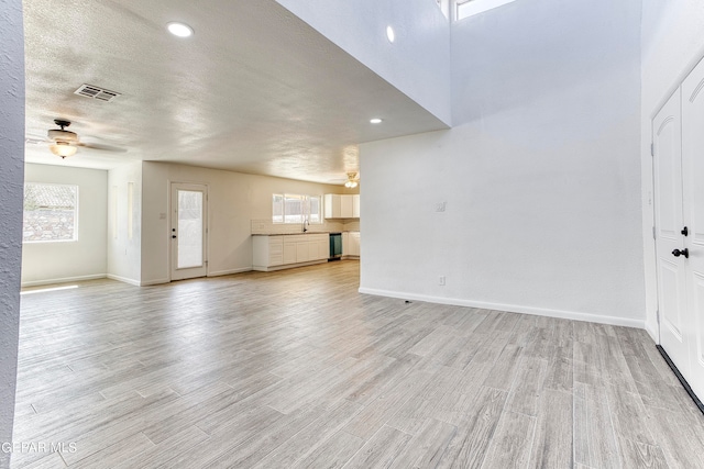 unfurnished living room with ceiling fan, a textured ceiling, sink, and light hardwood / wood-style floors