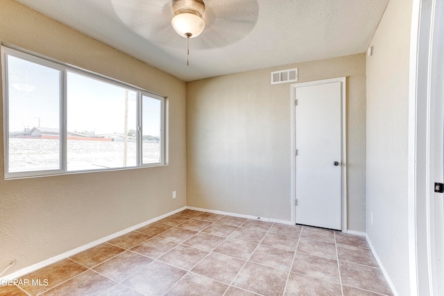 empty room with a textured ceiling, light tile patterned floors, and ceiling fan