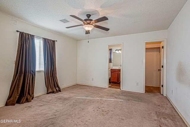 unfurnished bedroom featuring ceiling fan, light colored carpet, connected bathroom, and a walk in closet