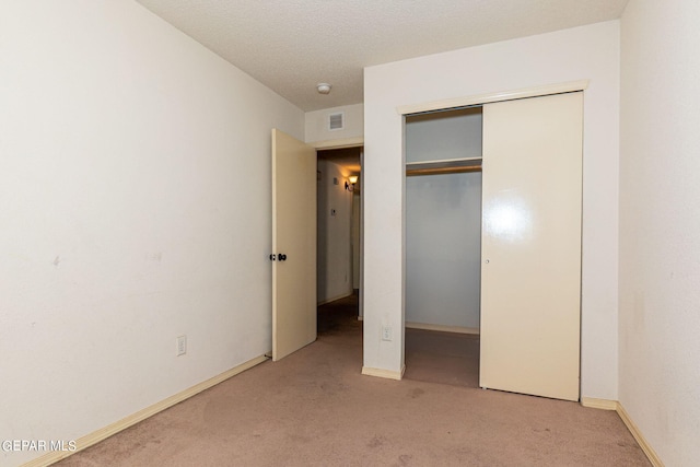 unfurnished bedroom featuring a closet, a textured ceiling, and light carpet