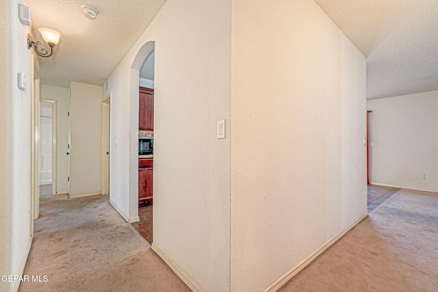 corridor with light carpet and a textured ceiling