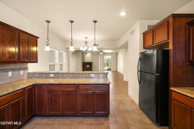 kitchen featuring black fridge, pendant lighting, kitchen peninsula, tasteful backsplash, and light stone countertops