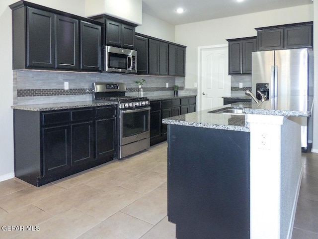 kitchen featuring a center island with sink, sink, stainless steel appliances, and tasteful backsplash