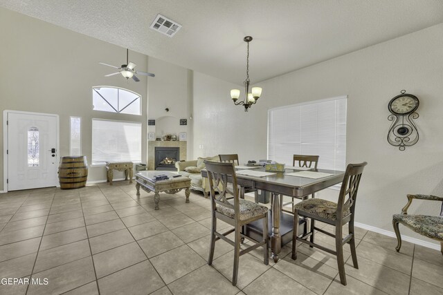 14241 Craggy Rock Ave, El Paso, TX 79938 - tiled dining space with visible vents, baseboards, a towering ceiling, a tiled fireplace, and ceiling fan with notable chandelier