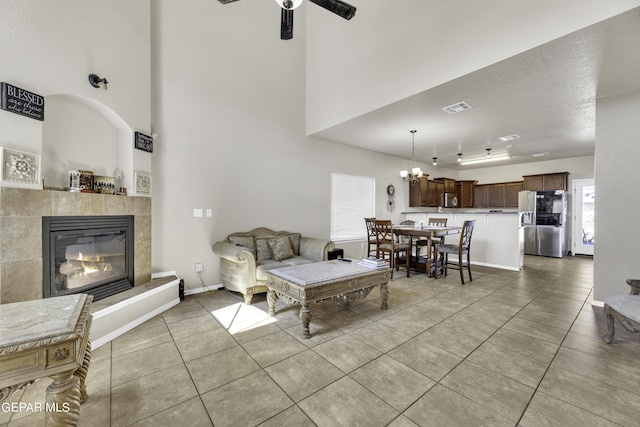 14241 Craggy Rock Ave, El Paso, TX 79938 - living room featuring ceiling fan with notable chandelier, a fireplace, visible vents, light tile patterned flooring, and a towering ceiling