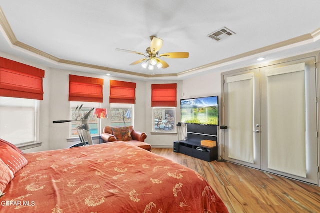 bedroom with a raised ceiling, crown molding, and light wood-type flooring