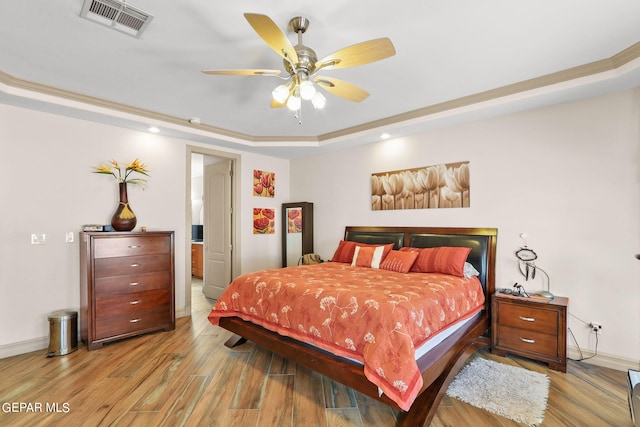 bedroom featuring light hardwood / wood-style floors, a tray ceiling, crown molding, and ceiling fan