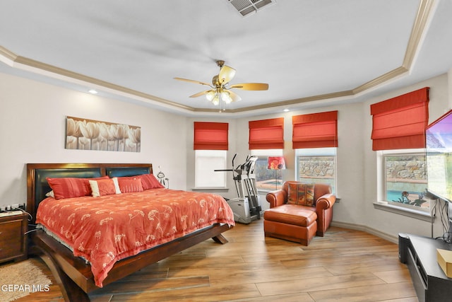 bedroom featuring light hardwood / wood-style floors, a tray ceiling, ornamental molding, and ceiling fan