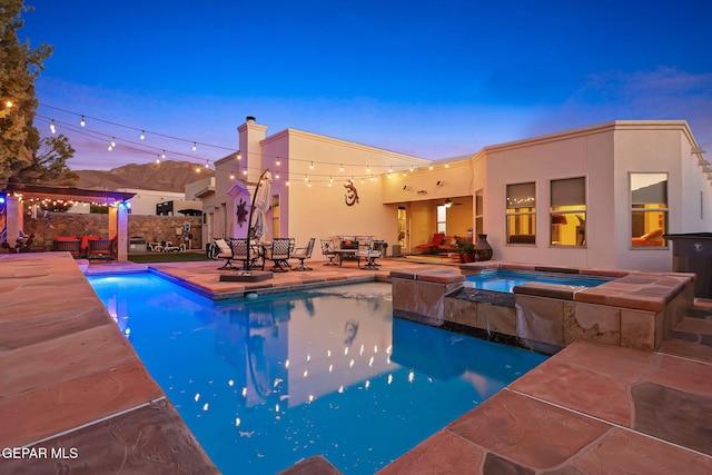 pool at dusk with an in ground hot tub and a patio area