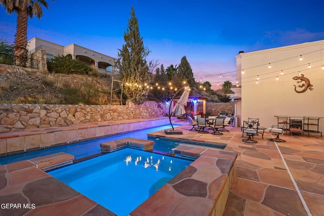 pool at dusk featuring an in ground hot tub and a patio area