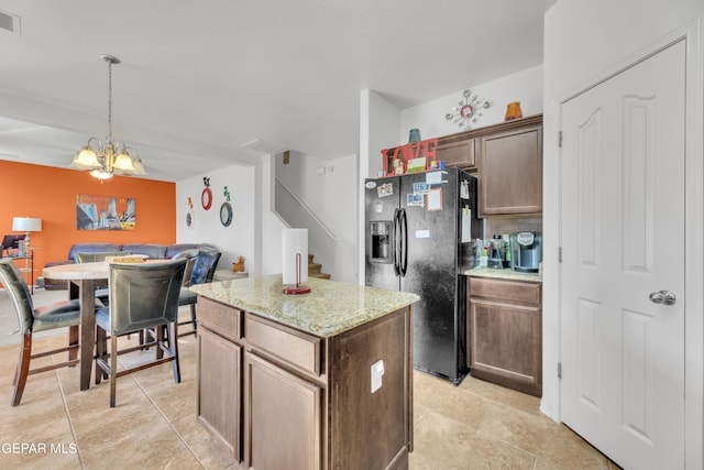 kitchen with a chandelier, black fridge with ice dispenser, light stone countertops, hanging light fixtures, and a center island