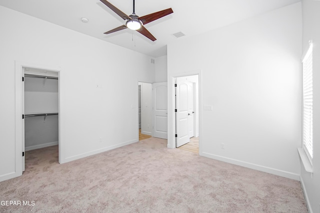 unfurnished bedroom with a closet, light colored carpet, a walk in closet, and ceiling fan