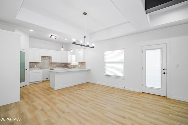 kitchen featuring hanging light fixtures, kitchen peninsula, tasteful backsplash, white cabinetry, and light hardwood / wood-style floors