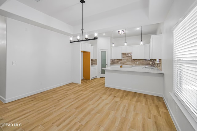 kitchen with a chandelier, light wood-type flooring, backsplash, hanging light fixtures, and white cabinetry