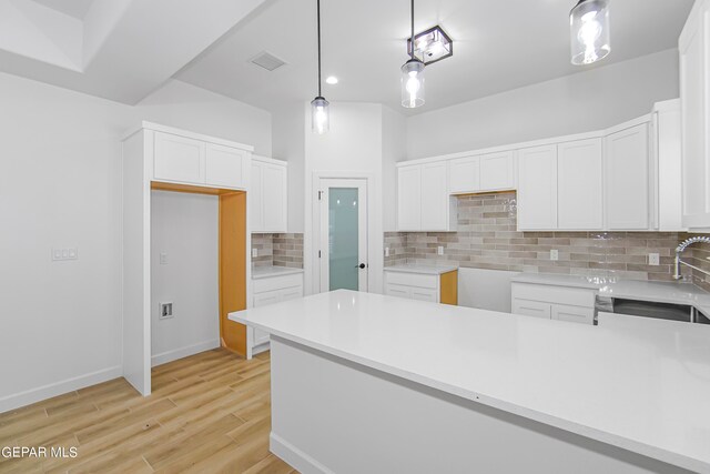 kitchen with light wood-type flooring, pendant lighting, sink, decorative backsplash, and white cabinets