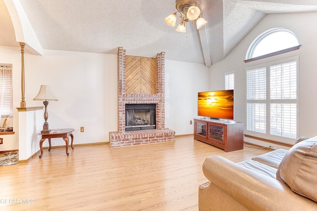 living room with ceiling fan, hardwood / wood-style flooring, a fireplace, vaulted ceiling, and a textured ceiling