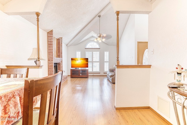 bedroom with lofted ceiling with beams, ceiling fan, a fireplace, light hardwood / wood-style flooring, and a textured ceiling