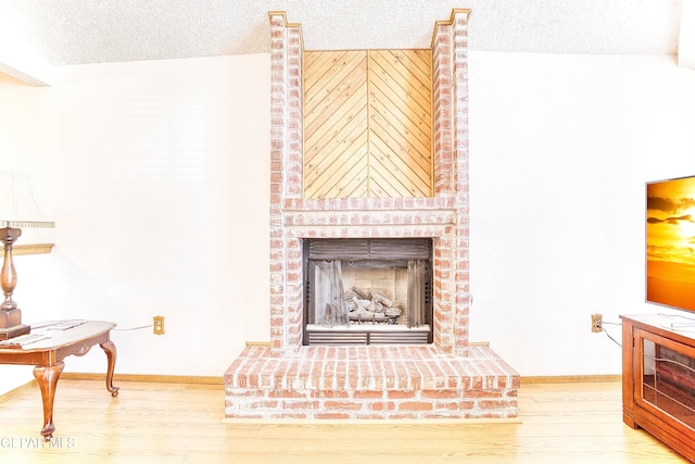 living room with a brick fireplace, wood-type flooring, and a textured ceiling