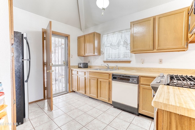 kitchen featuring sink, black refrigerator, vaulted ceiling, white dishwasher, and light tile patterned floors