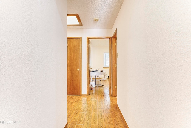 corridor featuring a skylight, a textured ceiling, and light hardwood / wood-style floors