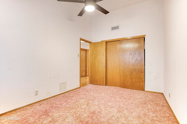 unfurnished bedroom featuring light carpet, a closet, a high ceiling, and ceiling fan