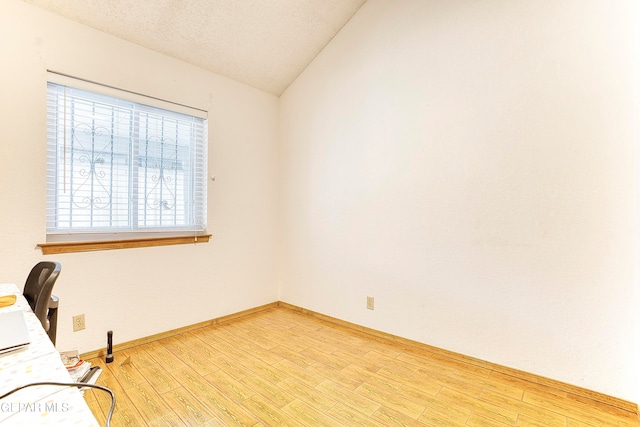 unfurnished office featuring lofted ceiling, light hardwood / wood-style flooring, and a textured ceiling