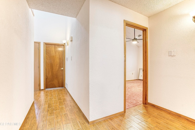 corridor with light wood-type flooring and a textured ceiling