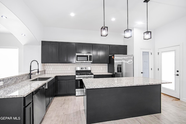 kitchen with hanging light fixtures, light hardwood / wood-style flooring, appliances with stainless steel finishes, a high ceiling, and light stone countertops