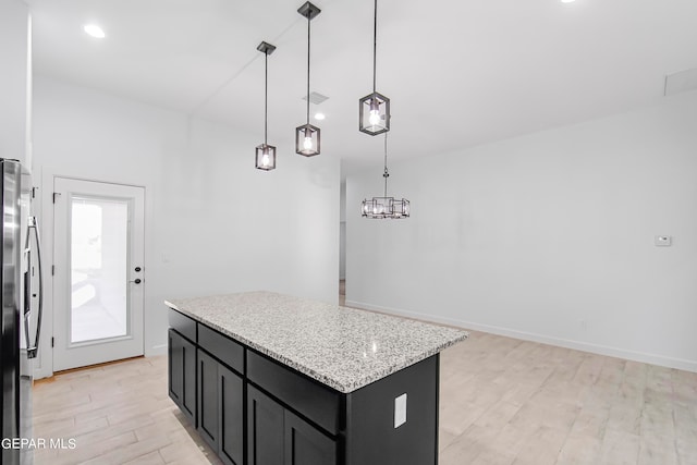 kitchen with light hardwood / wood-style floors, stainless steel refrigerator, pendant lighting, light stone countertops, and a center island