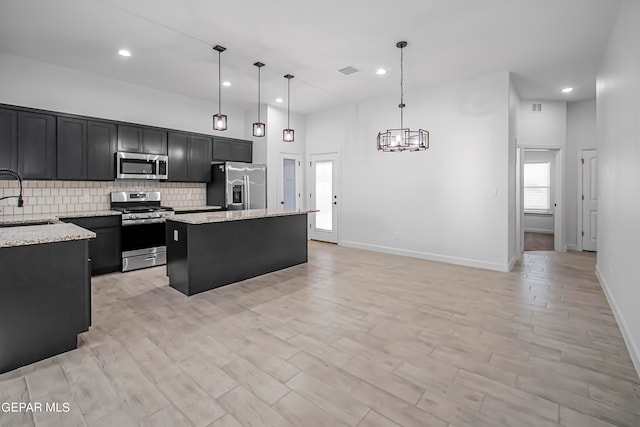 kitchen with light stone countertops, a center island, sink, appliances with stainless steel finishes, and decorative light fixtures