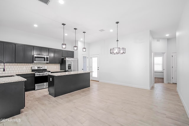 kitchen featuring a kitchen island, light stone countertops, stainless steel appliances, sink, and decorative light fixtures