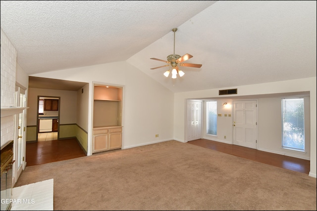 unfurnished living room with a brick fireplace, ceiling fan, vaulted ceiling, and light carpet