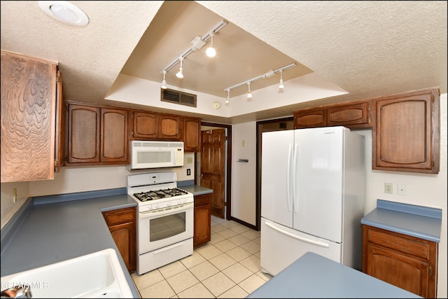 kitchen featuring white appliances, a tray ceiling, track lighting, sink, and a textured ceiling