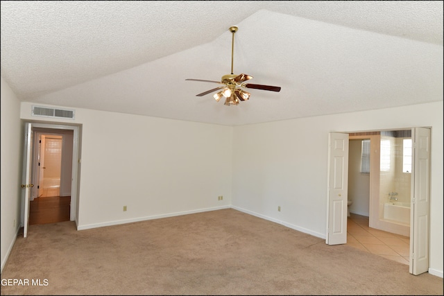 unfurnished bedroom featuring ceiling fan, light carpet, vaulted ceiling, ensuite bath, and a textured ceiling