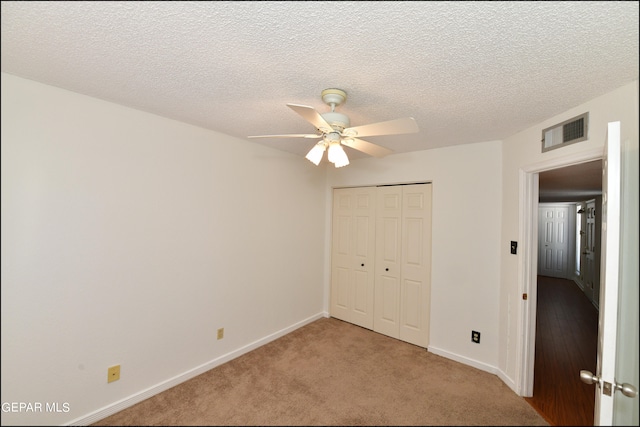 unfurnished bedroom featuring ceiling fan, a textured ceiling, a closet, and light carpet