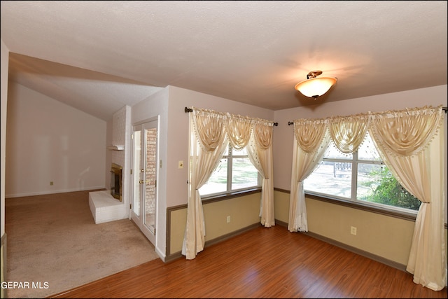 spare room with lofted ceiling, a brick fireplace, hardwood / wood-style flooring, and a textured ceiling