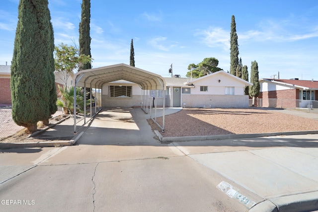 view of front facade featuring driveway, brick siding, fence, and a carport