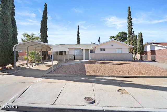 view of front facade featuring brick siding, driveway, fence, and a carport